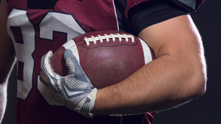 portrait of confident American football players holding ball while standing on field at nightの写真素材