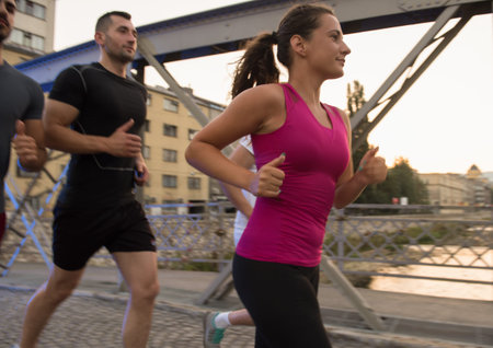 group of young sporty people jogging across the bridge at sunny morning in the cityの写真素材