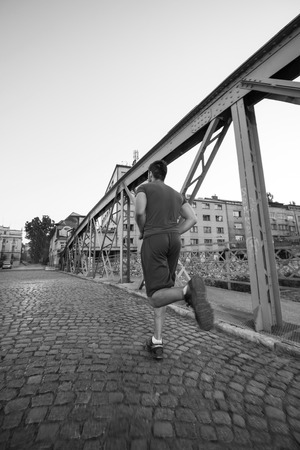 young sporty man jogging across the bridge at sunny morning in the cityの写真素材