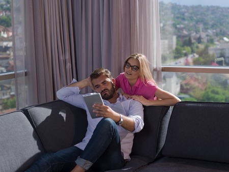 Young couple relaxing at  home using tablet computers reading in the living room on the sofa couch.の写真素材