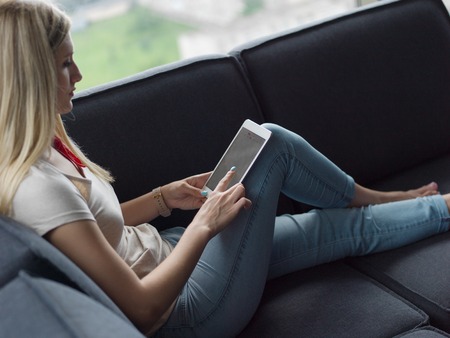 beautiful young woman on sofa at home surfing  internet using tablet computerの写真素材