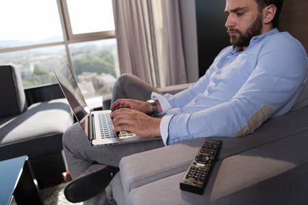 technology, home and lifestyle concept  of man working from home using laptop computer and sitting on sofaの写真素材