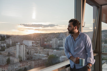 young man enjoying evening coffee and beautiful sunset landscape of the city while standing by the...