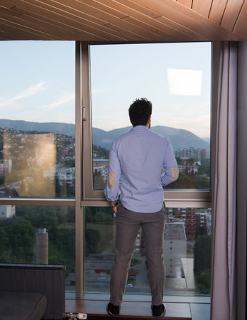 young man enjoying evening coffee and beautiful sunset landscape of the city while standing by the...