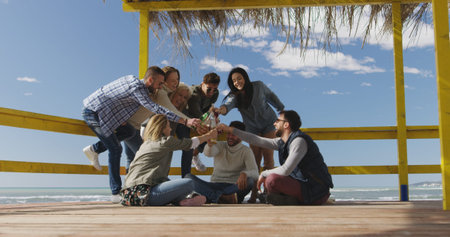 Happy Group Of Friends Hanging Out At Beach House having fun and drinking beer on autumn day