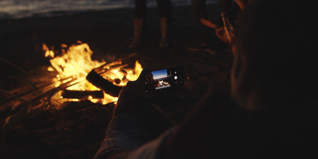 Boy Shows Girl A Picture On His Phone beside campfire on beachの写真素材