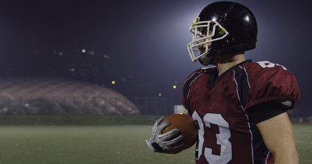 American football player holding ball while running on field at nightの写真素材