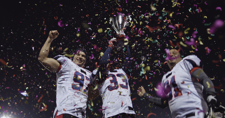 happy american football team celebrating victory with trophy and confetti on the night fieldの写真素材