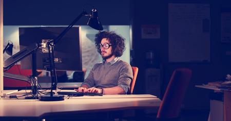 Young man working on computer at night in dark office. The designer works in the later time.の写真素材