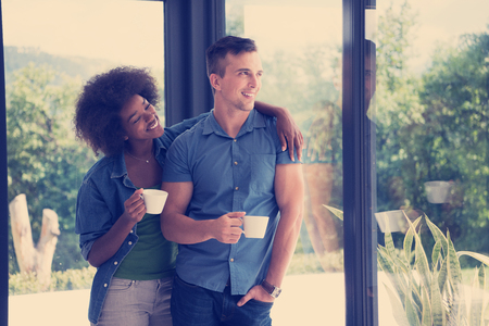 romantic happy young multiethnic couple enjoying morning coffee by the window in their luxury homeの写真素材