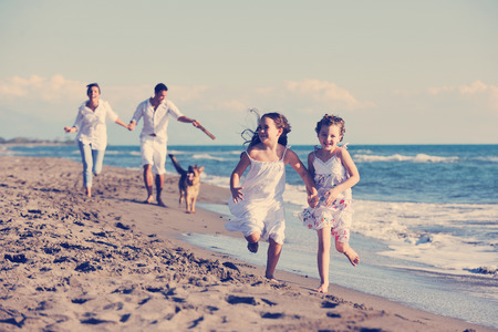happy young family in white clothing have fun and play with beautiful dog at vacations on beautiful beach の写真素材