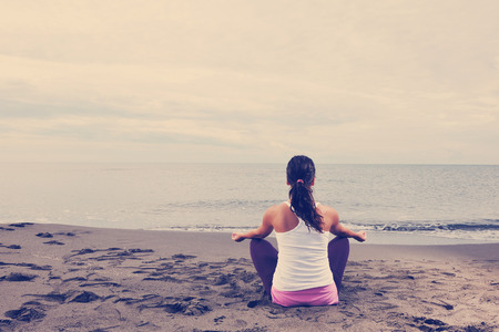 young woman meditating yoga in lotus positin on the beach at early morningの写真素材