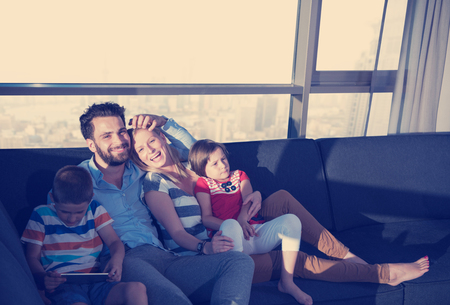 happy couple spending time with kids using tablet computer on sofa at homeの写真素材