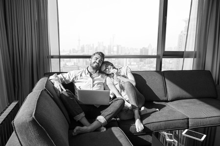 Young couple relaxing at  home using laptop computers reading in the living room near the window on the sofa couch.の写真素材