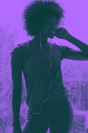 portrait of young afro american woman in gym on workout break while listening music on earphone  and dancing  rainy day and bad weather outdooor duo tone filterの写真素材