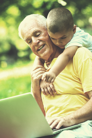 happy elderly senior grandfather and child in park using laptop computerの写真素材