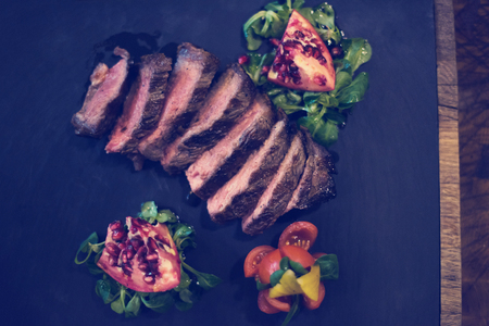 Juicy slices of grilled steak  with vegetables on a wooden board, top viewの写真素材