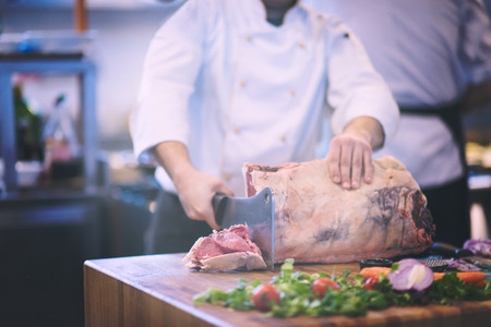 chef using ax while cutting big piece of beef  on wooden board in restaurant kitchenの写真素材