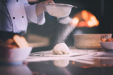 chef sprinkling flour over fresh pizza dough on kitchen tableの写真素材