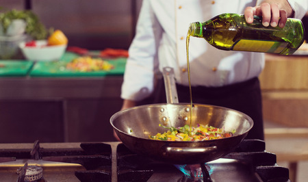 Young male chef flipping vegetables in wok at commercial kitchenの写真素材