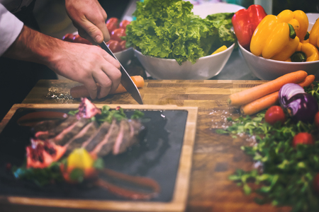 closeup of Chef hands in hotel or restaurant kitchen serving beef steak with vegetable decorationの写真素材