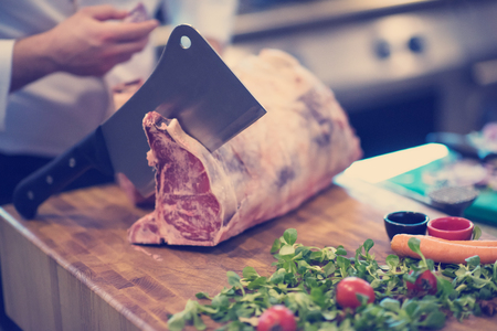 chef using ax while cutting big piece of beef  on wooden board in restaurant kitchenの写真素材