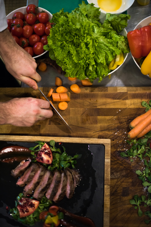 top view of Chef hands in hotel or restaurant kitchen serving beef steak with vegetable decorationの写真素材