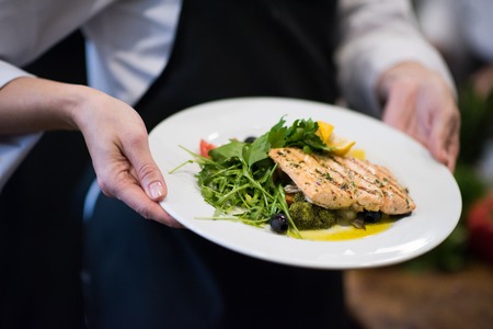 Chef hands holding fried Salmon fish fillet with vegetables for dinner in a restaurant kitchenの写真素材