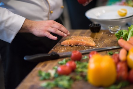 Chef hands preparing marinated Salmon fish fillet for frying in a restaurant kitchenの写真素材
