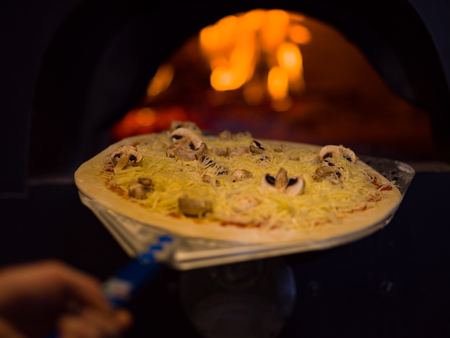 chef putting delicious pizza to brick wood oven with firewood and flameの写真素材
