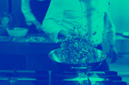 Young male chef flipping vegetables in wok at commercial kitchen