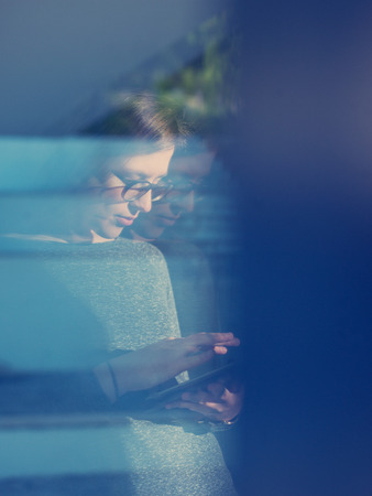 Woman using tablet computer at home, close up shot through windowの写真素材