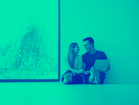 Young couple using laptop computer on the floor at luxury home together, looking at screen, smiling.の写真素材
