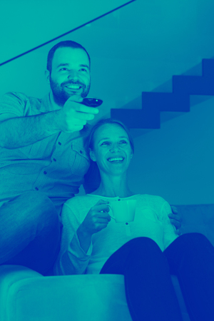 happy romantic couple watching television together in their luxury homeの写真素材