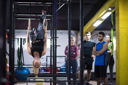 young athletic woman working out with personal trainer on gymnastic rings at the cross fitness gymの写真素材