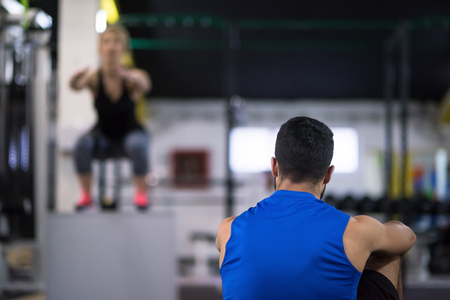 young athletic woman training with personal trainer  jumping on fit box at cross fitness gymの写真素材