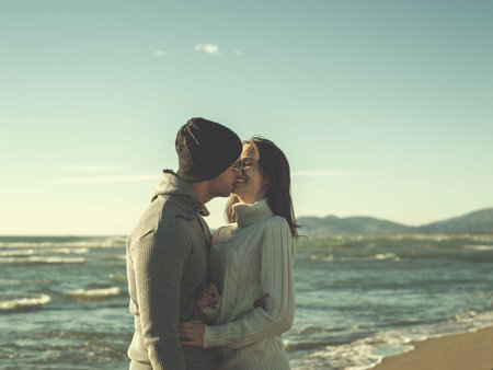 Young couple having fun walking and hugging on beach during autumn sunny day colored filter