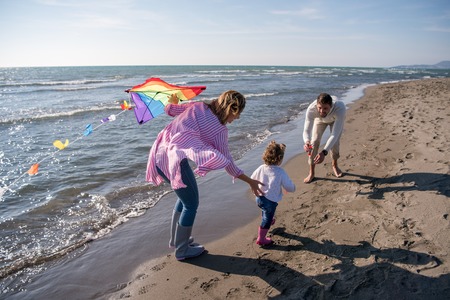young family with kids resting and having fun with a kite at beach during autumn dayの写真素材
