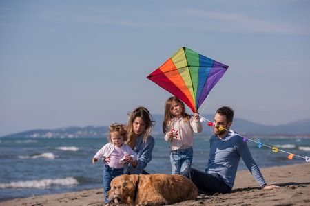 happy young family with kids having fun with a dog and  kite at beach during autumn dayの写真素材