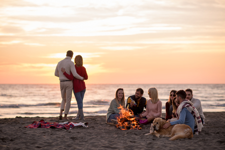Young Couple enjoying with friends Around Campfire on The Beach At sunset drinking beerの写真素材