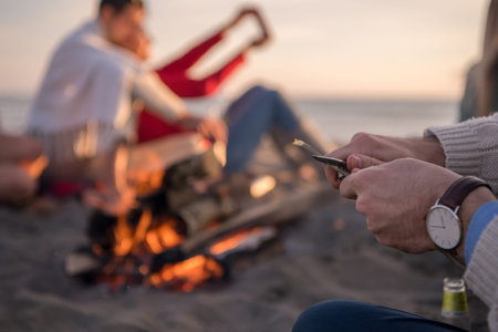 Happy Carefree Young Friends Having Fun And Drinking Beer By Bonefire On The Beach As The Sun Begins...