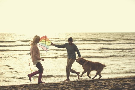 Young Couple having fun playing with a dog and Kite on the beach at autumn day filterの写真素材