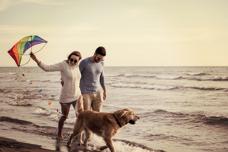 Young Couple having fun playing with a dog and Kite on the beach at autumn day filterの写真素材