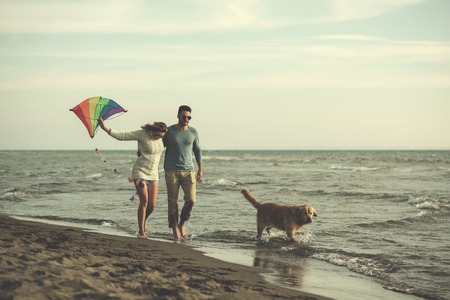 Young Couple having fun playing with a dog and Kite on the beach at autumn day filterの写真素材