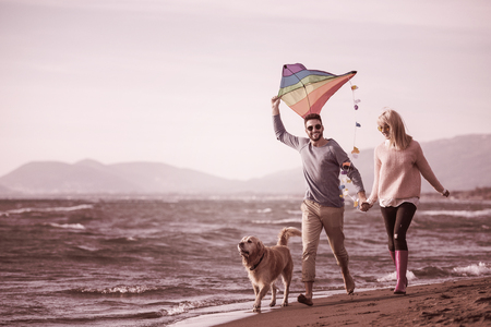 Young Couple having fun playing with a dog and Kite on the beach at autumn day filterの写真素材