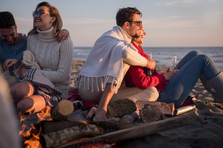 Young Couple enjoying with friends Around Campfire on The Beach At sunset drinking beerの写真素材