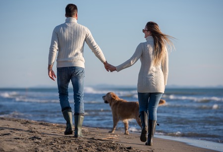 Couple Running On The Beach Holding Their Hands with dog On autmun dayの写真素材