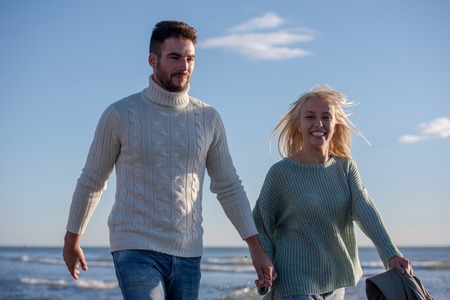 Young couple having fun walking and hugging on beach during autumn sunny dayの写真素材
