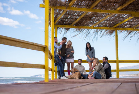 Happy Group Of Friends Hanging Out At Beach House having fun and drinking beer on autumn day