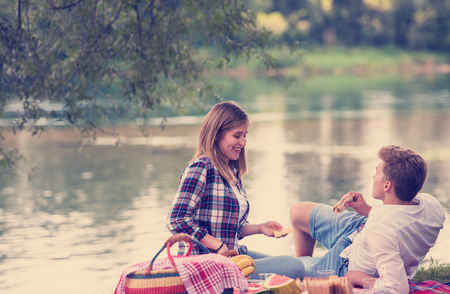 Couple in love enjoying picnic time drink and food in beautiful nature on the river bankの写真素材